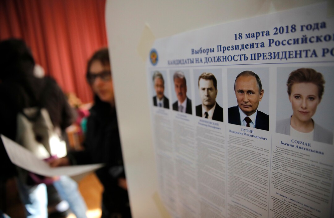 Voters walk past a poster showing the candidates in the presidential election in Moscow, Russia, Sunday, March 18, 2018. Russians are voting in a presidential election in which Vladimir Putin is seeking a fourth term in the Kremlin. (AP Photo/Pavel Golovkin)
