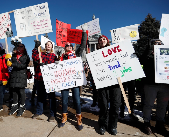 From left, Caitlin Weber, Abby Kloberdanz ad Chelsea Geier, all teachers at Bear Valley International School, wave placards during a strike rally on the west steps of the state Capitol, Monday, Feb. 11, 2019, in Denver. The strike is the first for teachers in Denver since 1994 and centers on base pay. (AP Photo/David Zalubowski)