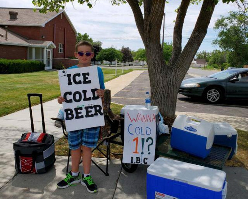 (Brigham City Police Department via AP) Seth Parker stands at his soda stand in Brigham City, Utah, on Tuesday, July 16, 2019. Parker is earning widespread social media attention for his neighborhood soda stand thanks to a sign he holds that reads, "Ice cold beer" with "root" above the word beer in tiny print. Brigham City Police Lt. Tony Ferderber said Thursday, July 18, 2019, that several residents in the northern Utah city called police concerned about a young boy selling alcohol in front of a church. Officers realized that it was just a clever marketing ploy and posted pictures of 11-year-old Seth Parker on Facebook with the comment, "a twist on a lemonade stand."