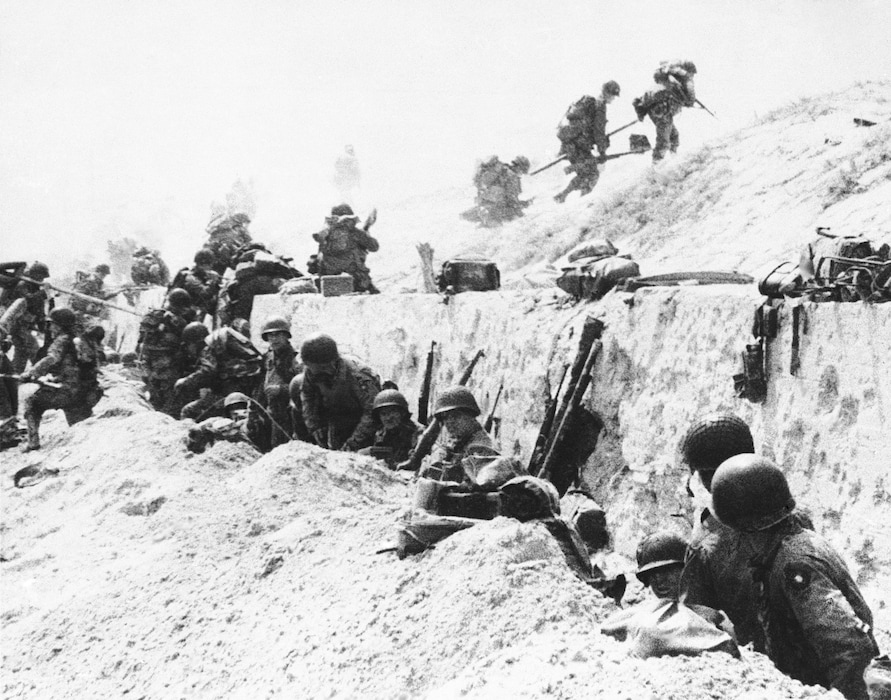 (AP) Troops on Utah Beach in Normandy, France on June 9, 1944, take shelter behind a sea wall while awaiting orders to move inland during the invasion by allied troops.