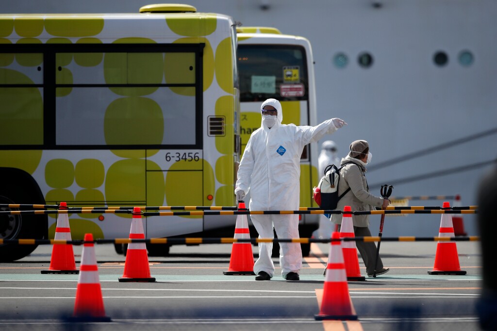 (Jae C. Hong | AP) An unidentified passenger is directed in a parking lot after disembarking from the quarantined Diamond Princess cruise ship Wednesday, Feb. 19, 2020, in Yokohama, near Tokyo. Passengers tested negative for COVID-19 started disembarking Wednesday.