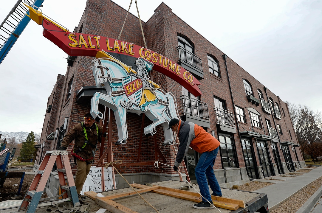 (Francisco Kjolseth  |  The Salt Lake Tribune)  The Salt Lake Costume Co. sign, originally designed by Lloyd S. Coley in the '50s while working for Rainbow Neon Sign Co., lives on once more as Sergio Camacho, left, and Don Fitches help put it back home in its original location at 1700 S. 1100 East on Monday, Dec. 23, 2019, in what is now called the Salt Lake Costume Apartments.