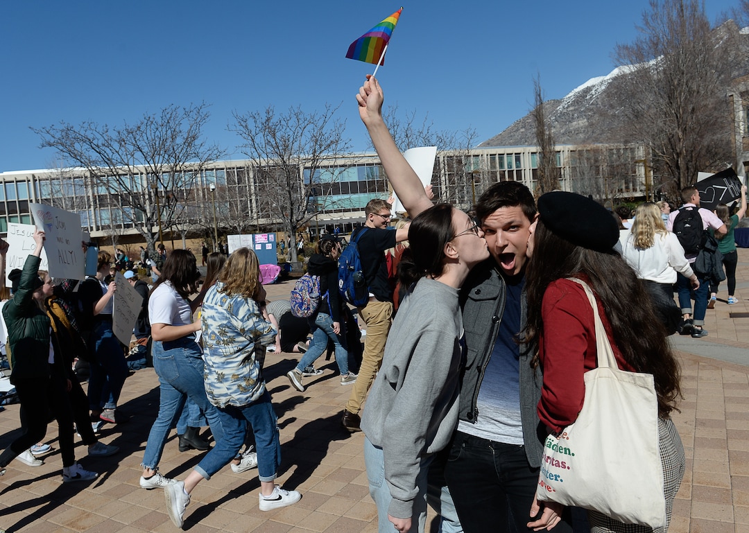 (Francisco Kjolseth  |  The Salt Lake Tribune) Jake Taylor gets a kiss from friends Julia Stark, left, and Sophie Gordon as they join other students protesting outside the student center at Brigham Young University in Provo, Wednesday, March 4, 2020, after an official with The Church of Jesus Christ of Latter-day Saints issued a clarification to the school's Honor Code, which said that same-sex romantic behavior is still "not compatible" with the rules at BYU.