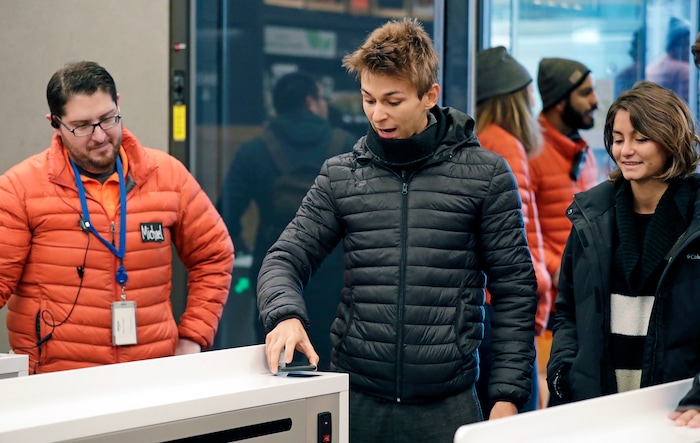 As an Amazon Go worker, left, looks on to offer assistance, Tadeo Klappenbach, center, uses an Amazon Go app just put on his cellphone to enter the store with his five family members, Monday, Jan. 22, 2018, in Seattle. Klappenbach and his family, of Buenos Aires, Argentina, were visiting the area and made a point to stop in the artificial intelligence-powered store on its opening day. (AP Photo/Elaine Thompson)