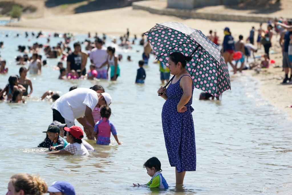 (Marcio Jose Sanchez | The Associated Press) A visitors shields herself with from the sun with an umbrella in the swimming beach at Castaic Lake on Saturday, Sept. 5, 2020, in Castaic, Calif. California is sweltering under a dangerous Labor Day weekend heat wave that was expected to spread triple-digit temperatures over much of the state while throngs of people might spread the coronavirus by packing beaches and mountains for relief.