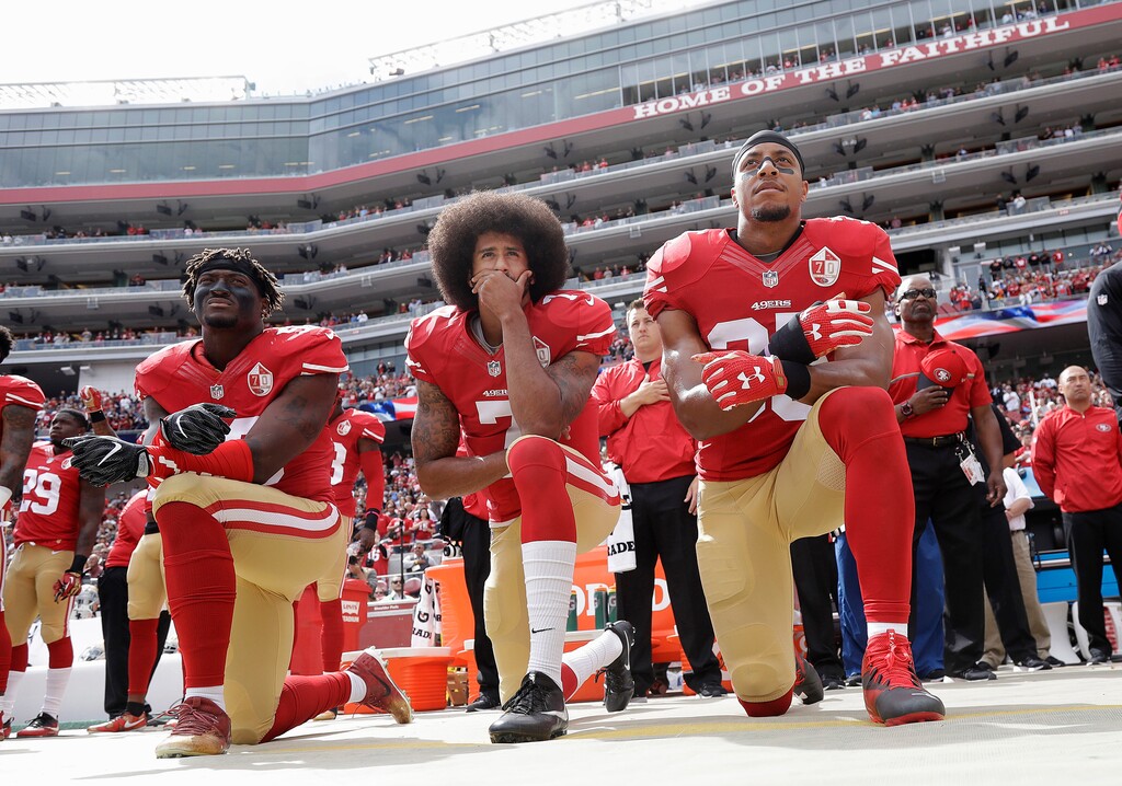 FILE - In this Oct. 2, 2016, file photo, from left, San Francisco 49ers outside linebacker Eli Harold, quarterback Colin Kaepernick, center, and safety Eric Reid kneel during the national anthem before an NFL football game against the Dallas Cowboys in Santa Clara, Calif. What started as a protest against police brutality has mushroomed a year later into a divisive debate over the future of Kaepernick who refused to stand for the national anthem and now faces what his fans see as blackballing for speaking out in a country roiled by racial strife. The once-rising star and Super Bowl quarterback has been unemployed since March, when he opted out of his contract and became a free agent who could sign with any team. (AP Photo/Marcio Jose Sanchez, File)