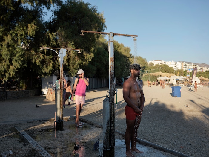 (Myrto Papadopoulos | The New York Times) Hasib Hotak, a homeless refugee from Afghanistan, uses the public showers at a beach in Athens, Greece, July 22, 2020. Around the world, the poor and marginalized are much more likely to be vulnerable to extreme heat; Hasib sleeps with other refugees on a rooftop that turns blazing hot by midday.