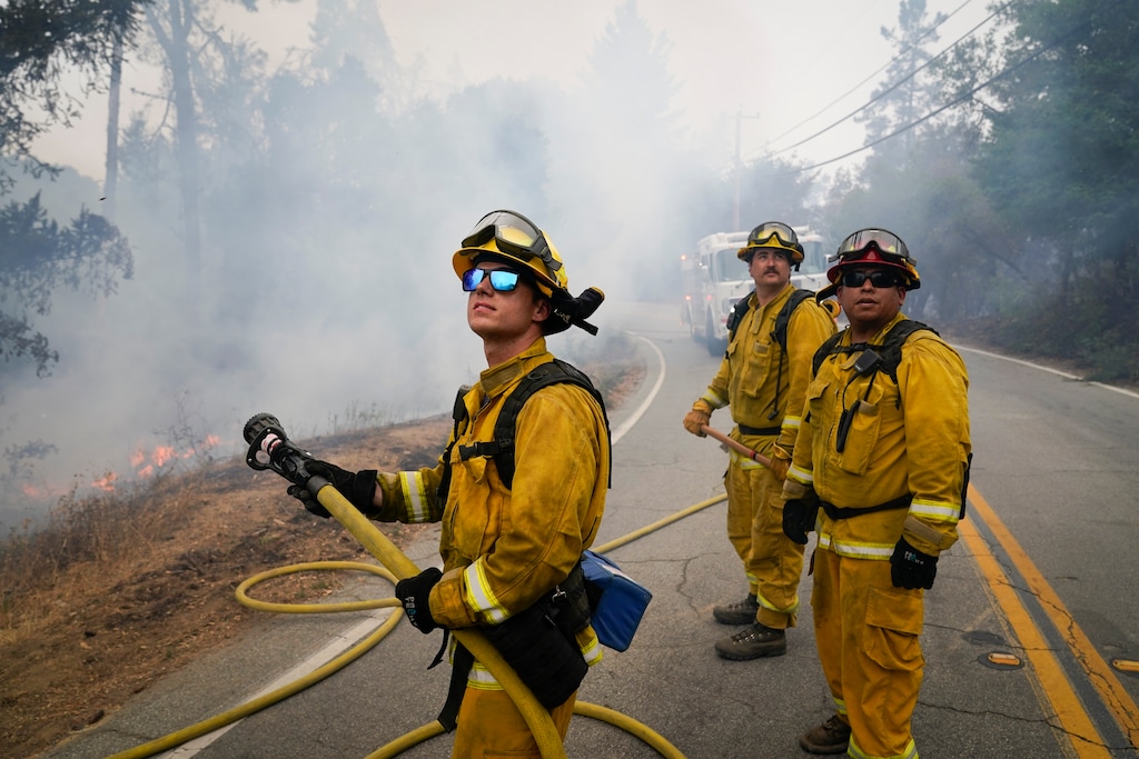 (Marcio Jose Sanchez | The Associated Press) Firefighters Cody Nordstrom, Kyle Harp and Robert Gonzalez, from left, of the North Central Fire station out of Kerman, Calif., look up at a water-dropping helicopter while fighting the CZU Lightning Complex Fire on Sunday, Aug. 23, 2020, in Bonny Doon, Calif.