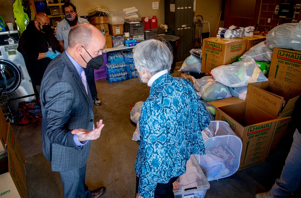 (Isaac Hale | Special to The Tribune) Donated items await to be sorted as Gov. Spencer Cox talks with philanthropist Pamela Atkinson before a press conference held at The Road Home Midvale Family Center on Tuesday, March 2, 2021.