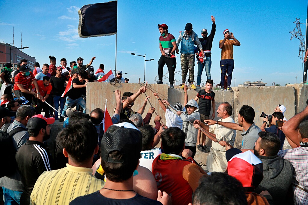 (Hadi Mizban | AP) Anti-government protesters pull down concrete walls leading to the heavily guarded Green Zone during a demonstration in central Baghdad, Iraq, Friday, Oct. 25, 2019. Iraqi police fired live shots into the air and dozens of tear gas canisters on Friday to disperse thousands of protesters on the streets of Baghdad, sending young demonstrators running for cover and covering the capital's bridge with thick white smoke.