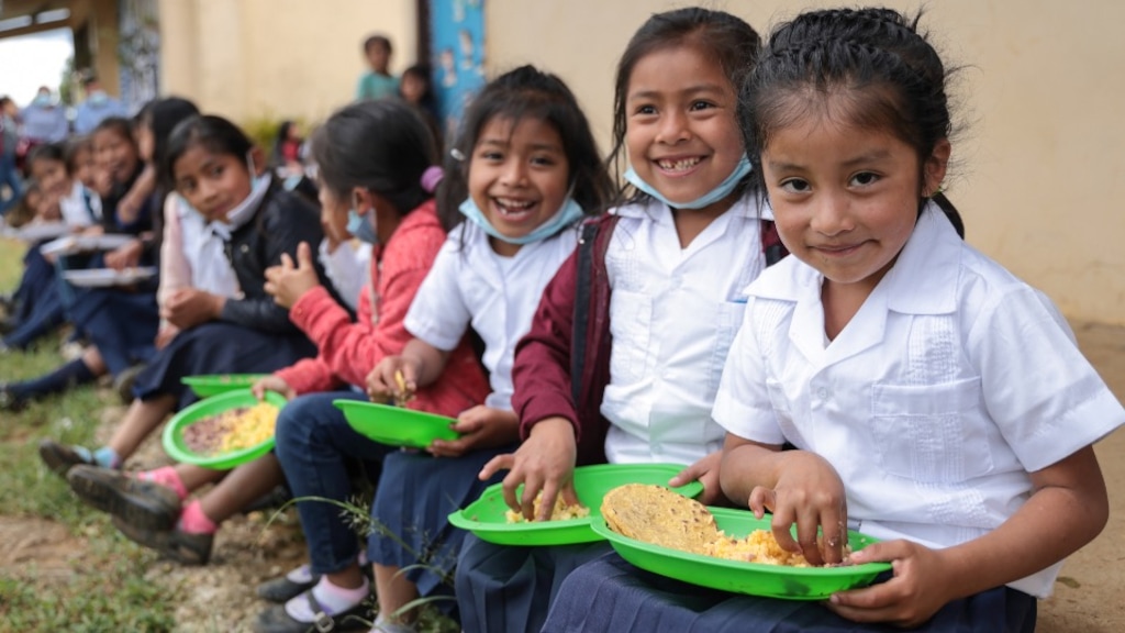 (Catholic Relief Services) Madelyn Sofia Mendez Mateo (far right), a first grader in Planes de Rio Grande, Honduras, eats her meal during recess time with her classmates. “I love it when they serve spaghetti, tortillas, beans and rice,” said Sofía, who dreams of becoming a teacher or an engineer. The Church of Jesus Christ is supporting the efforts of Catholic Relief Services in various countries to provide girls and young women with nutrition education and counseling, along with nutritious supplements and food.