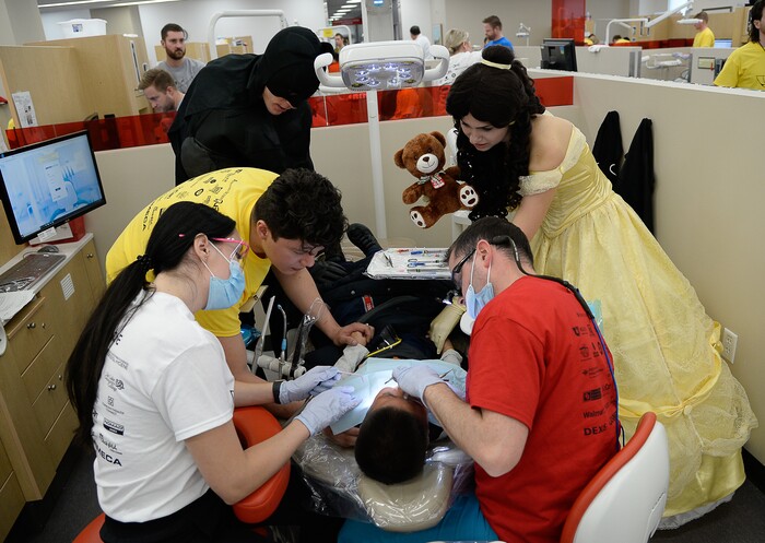 (Francisco Kjolseth  |  The Salt Lake Tribune) Karlee Chipman, left, and Roberto Ramirez assist Dr. Aaron Roundy, as a patient having a rough go with four new fillings gets extra care and attention from Batman played by Tyson Jeppson and Belle played by Marina McNeill during the American Dental AssociationÕs ÒGive Kids a SmileÓ program at the University of Utah on Saturday, Feb. 29, 2020. McNeill, a graduate of the U. started the group, Service Opportunities 101, 6 years ago and organized a team of volunteer superheroes and princesses to calm the nerves of young patients getting no-cost dental work.