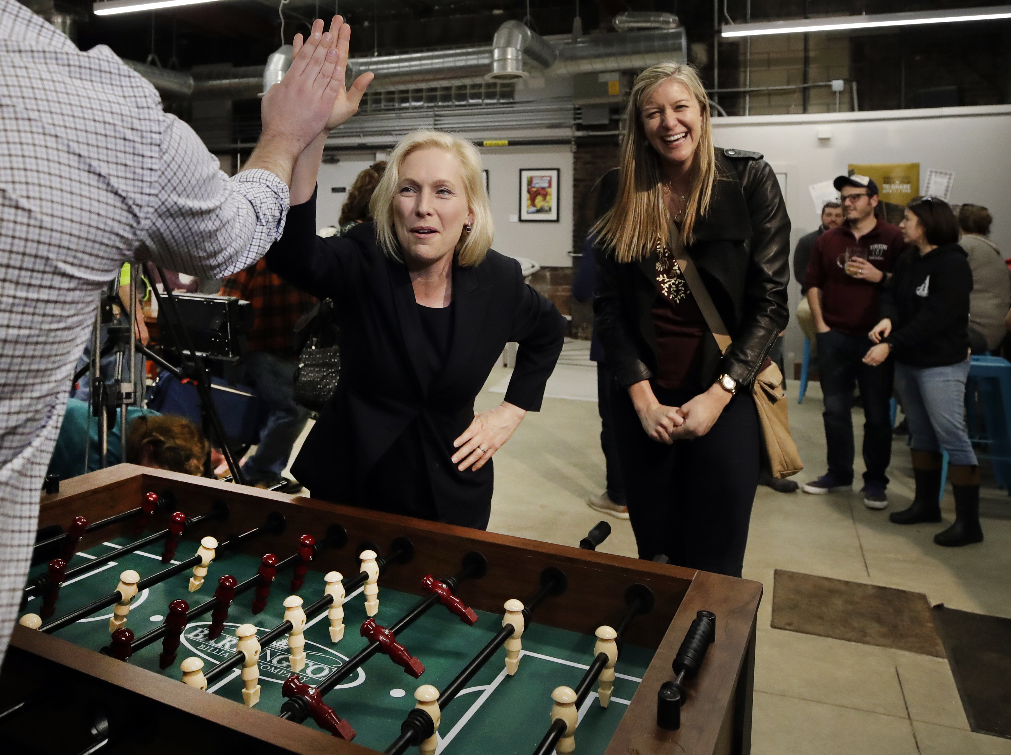(Elise Amendola | The Associated Press) Democratic presidential candidate Sen. Kirsten Gillibrand, D-N.Y., high-fives a foosball opponent as partner Casey Leach of Manchester, N.H., laughs at a campaign meet-and-greet, Friday, March 15, 2019, at To Share Brewing in Manchester, N.H.