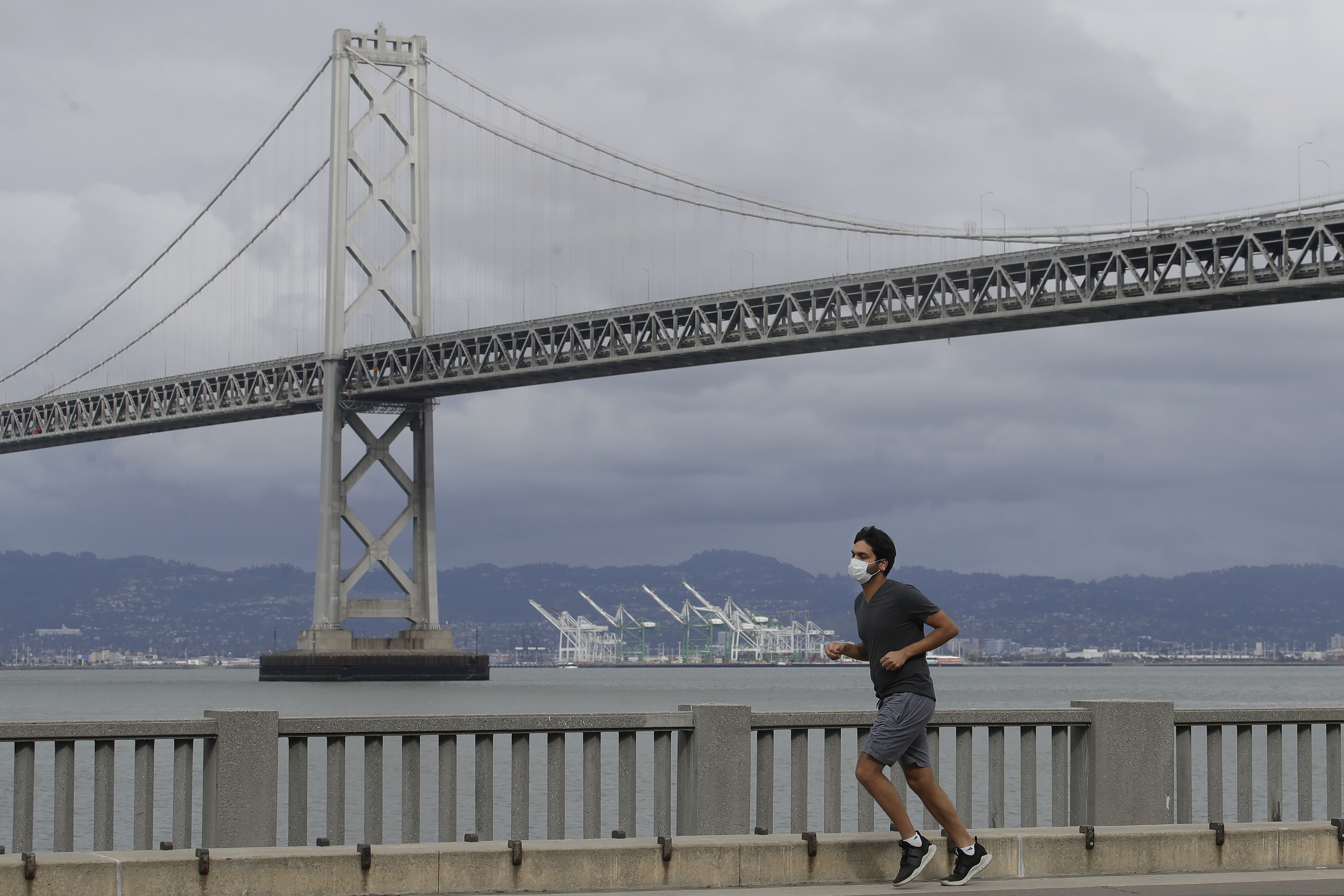 (Jeff Chiu | AP) A man wears a mask to protect himself from the coronavirus while running in front of the San Francisco-Oakland Bay Bridge along the Embarcadero in San Francisco, Sunday, April 5, 2020.