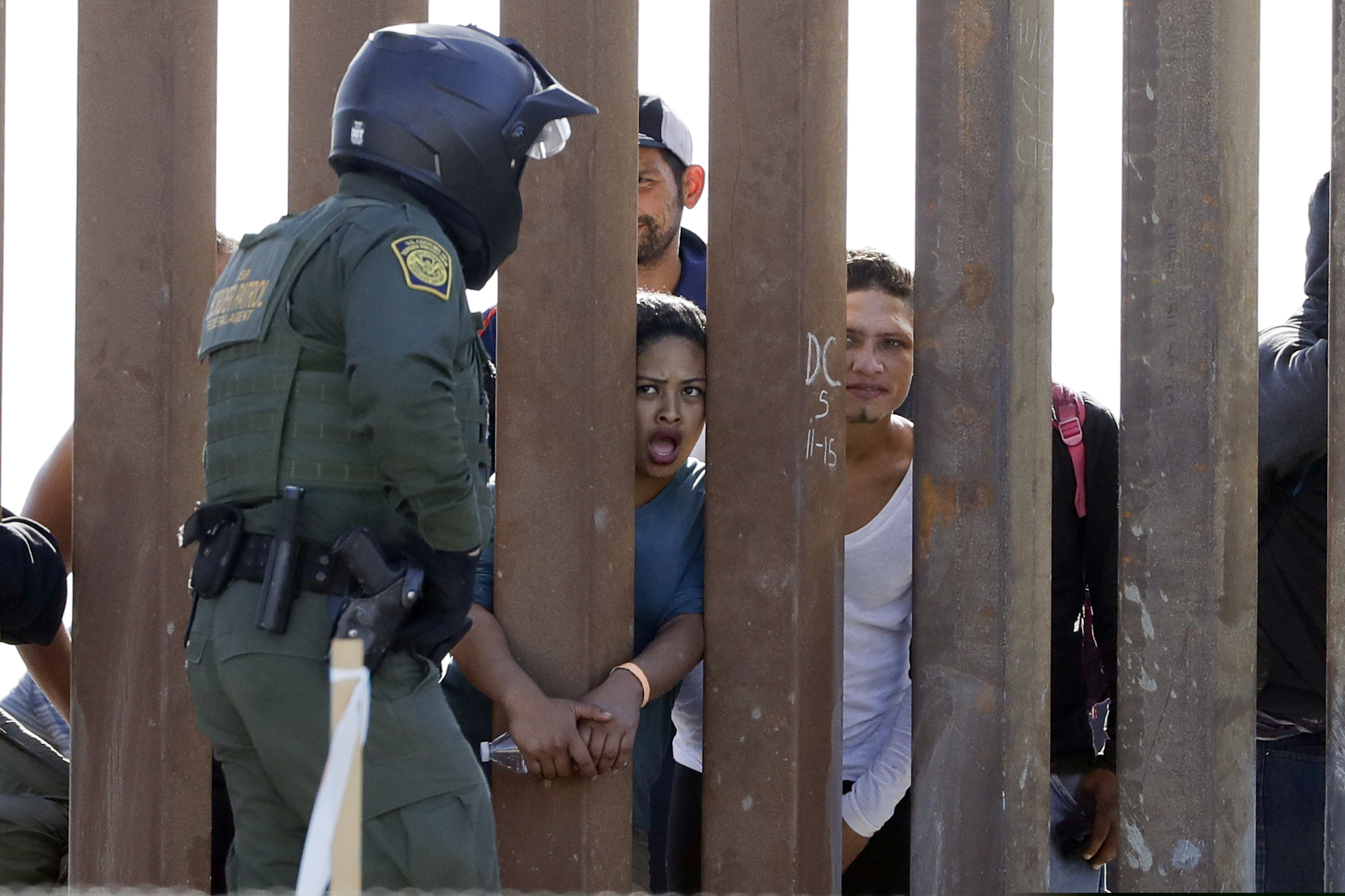 Migrants from Central America yell through a border wall at a U.S. Border Patrol agent after he pulled down a banner Sunday, Nov. 25, 2018, in San Diego. Migrants approaching the U.S. border from Mexico were enveloped with tear gas Sunday after a few tried to breach the fence separating the two countries. (AP Photo/Gregory Bull)