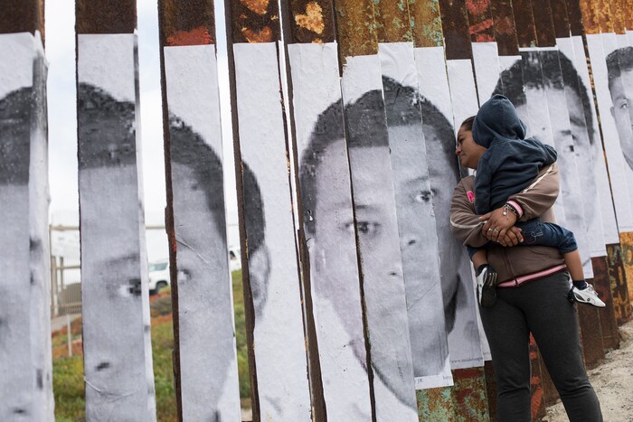 A member of the Central American migrant caravan, holding a child, looks through the border wall toward a group of people gathered on the U.S. side, near the beach where the border wall ends in the ocean, in Tijuana, Mexico, Sunday, April 29, 2018. U.S. immigration lawyers are telling Central Americans in a caravan of asylum-seekers that traveled through Mexico to the border with San Diego that they face possible separation from their children and detention for many months. They say they want to prepare them for the worst possible outcome. (AP Photo/Hans-Maximo Musielik)