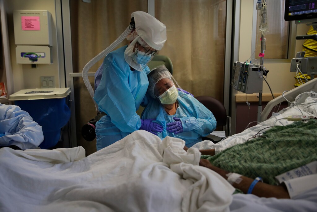 FILE - In this July 31, 2020, file photo, Romelia Navarro, right, is comforted by nurse Michele Younkin as she weeps while sitting at the bedside of her dying husband, Antonio, in St. Jude Medical Center's COVID-19 unit in Fullerton, Calif. The U.S. death toll from the coronavirus topped 200,000 Tuesday, Sept. 22, a figure unimaginable eight months ago when the scourge first reached the world’s richest nation with its sparkling laboratories, top-flight scientists and towering stockpiles of medicines and emergency supplies. (AP Photo/Jae C. Hong, File)