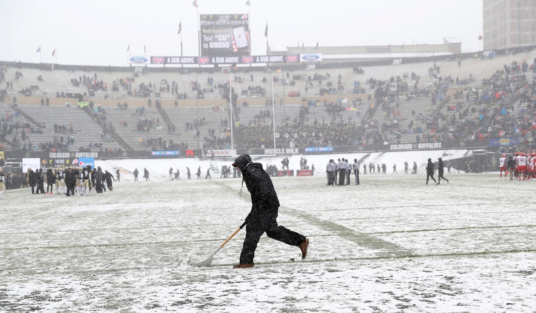 A grounds crew member uses a shovel to clear snow from the yard lines in the first half of an NCAA college football game between Utah and Colorado Saturday, Nov. 17, 2018, in Boulder, Colo. (AP Photo/David Zalubowski)