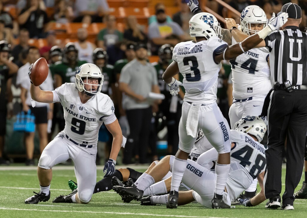 (Eugene Tanner | AP) Utah State linebacker David Woodward (9) holds up the football after intercepting a pass in the first half of an NCAA college football game, Saturday, Nov. 3, 2018, in Honolulu. Utah State safety Jontrell Rocquemore (3) signals his team has position of the football.