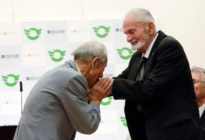 Tatsuya Yasue, left, kisses the hands of WWII veteran Marvin Strombo during a ceremony in Higashishirakawa, in central Japan's Gifu prefecture Tuesday, Aug. 15, 2017. Strombo returned a Japanese flag with autographed messages which was owned by Tatsuya's brother Sadao Yasue, who was killed in the Pacific during World Work II. (AP Photo/Eugene Hoshiko)