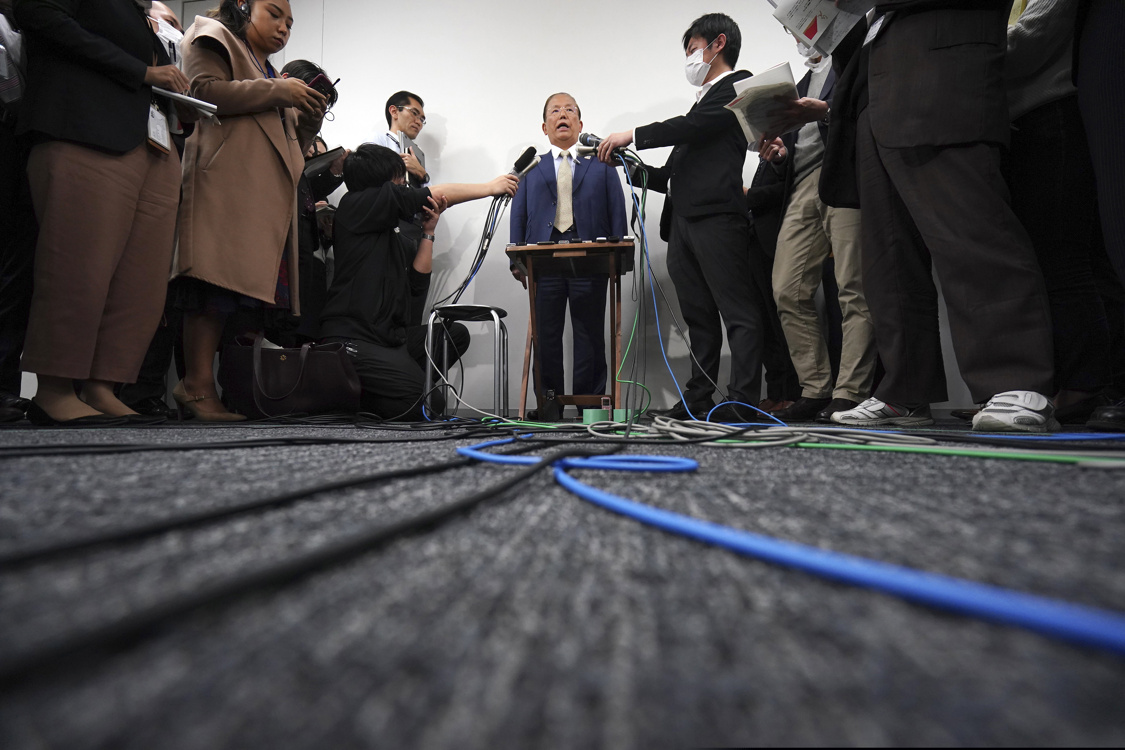 Toshiro Muto, CEO of the Tokyo 2020 Organizing Committee, is surrounded by journalists during a news conference in Tokyo Tuesday, March 17, 2020. Tokyo Olympic organizers are pushing ahead with the Japanese leg of the torch relay that opens on March 26 despite the threat of the spreading coronavirus. Muto said that crowds will not be prohibited from gathering on the roadside. But he asked for restraint and warned the relay could be stopped or delayed. (AP Photo/Eugene Hoshiko)