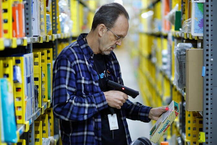 In this Wednesday, Dec. 20, 2017, photo, a clerk picks an item from a shelf and scans it with a hand-held device to fill a customer order at the Amazon Prime warehouse in New York. (AP Photo/Mark Lennihan)