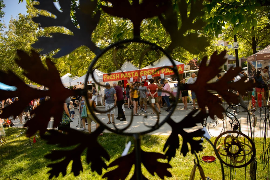 (Trent Nelson | The Salt Lake Tribune)Artwork by Steve Johnson frames a scene at the opening day of the 2018 Downtown Farmers Market at Pioneer Park in Salt Lake City, Saturday June 9, 2018.