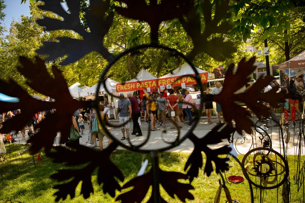 (Trent Nelson | Tribune file photo)
Artwork by Steve Johnson frames a scene at the opening day of the 2018 Downtown Farmers Market at Pioneer Park in Salt Lake City. This year, the arts and crafts section of the market has been eliminated due to coronavirus restrictions.