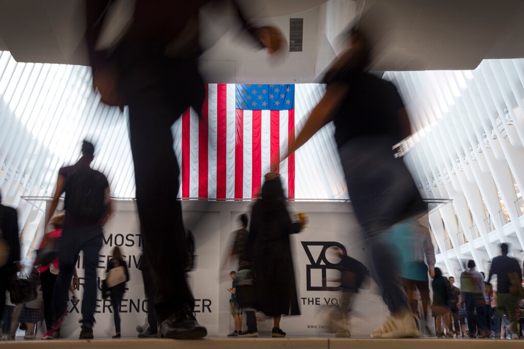 (Wong Maye-E | AP file photo)  People walk past an American flag at the start of a work day, at the Oculus, part of the World Trade Center transportation hub in New York., on Sept. 11, 2019.