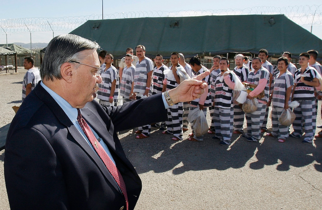 FILE - In this Feb. 4, 2009, file photo, Maricopa County Sheriff Joe Arpaio, left, orders approximately 200 convicted illegal immigrants handcuffed together and moved into a separate area of Tent City, for incarceration until their sentences are served and they are deported to their home countries, in Phoenix. An audit report produced in a racial profiling case against the Maricopa County Sheriff's Office says Hispanics are more likely to be searched and arrested by sheriff's deputies in traffic stops than white people. The report was issued nearly four years after a judge ordered a sweeping overhaul of then-Sheriff Joe Arpaio's office after concluding officers had racially profiled Hispanics in immigration patrols. (AP Photo/Ross D. Franklin, File)