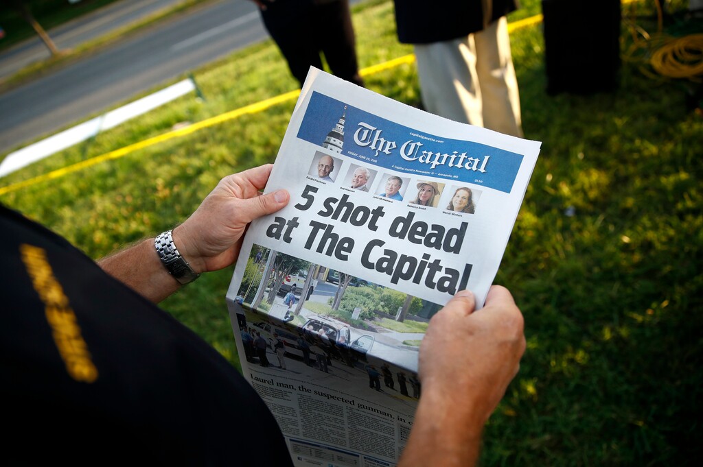 FILE - In this June 29, 2018, file photo, Steve Schuh, county executive of Anne Arundel County, holds a copy of the Capital Gazette near the scene of a shooting at the newspaper's office in Annapolis, Md. At a time when journalists are being branded “the enemy of the people,” staff members at the Capital Gazette newspaper are feeling renewed appreciation in their community, a year after a gunman went on a newsroom rampage that left five of their colleagues dead. (AP Photo/Patrick Semansky, File)