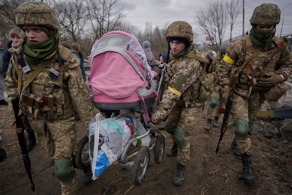 (Vadim Ghirda | AP) Ukrainian servicemen carry a baby stroller after crossing the Irpin river on an improvised path under a bridge that was destroyed by a Russian airstrike, while assisting people fleeing the town of Irpin, Ukraine, Saturday, March 5, 2022.