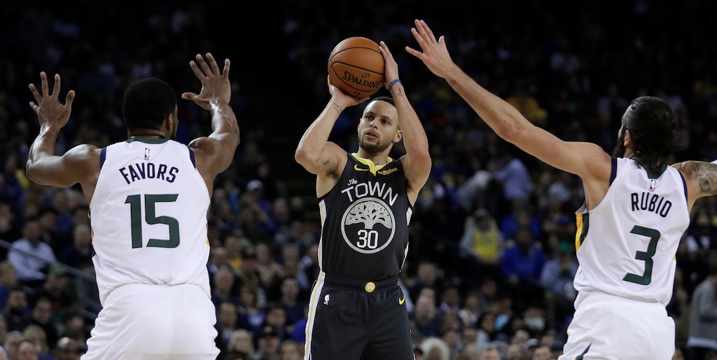 Golden State Warriors' Stephen Curry, center, shoots between Utah Jazz's Derrick Favors (15) and Ricky Rubio (3) during the second half of an NBA basketball game Tuesday, Feb. 12, 2019, in Oakland, Calif. (AP Photo/Ben Margot)