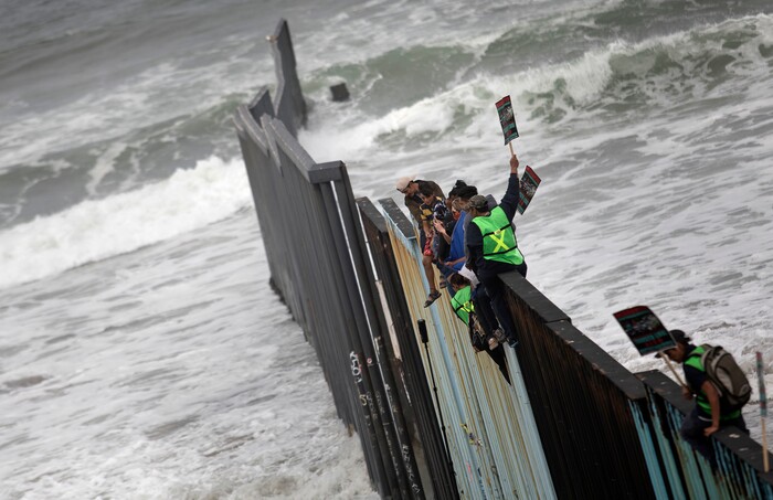 Central American migrants traveling with a caravan sit momentarily on top of the border wall during a gathering of migrants living on both sides of the border, on the beach where the border wall ends in the ocean, with Tijuana, Mexico at left and San Diego at right, Sunday, April 29, 2018. U.S. immigration lawyers are telling Central Americans in a caravan of asylum-seekers that traveled through Mexico to the border with San Diego that they face possible separation from their children and detention for many months. They say they want to prepare them for the worst possible outcome. (AP Photo/Hans-Maximo Musielik)