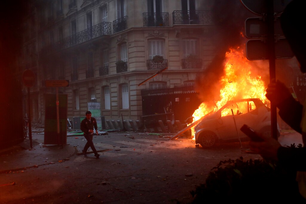A demonstrator runs past a burning car during a demonstration in Paris on Saturday, Dec. 1, 2018, against an increase in fuel taxes. Even proponents of carbon taxes acknowledge that an increase in fuel taxes can disproportionally hurt low-income people. Energy costs make up a larger portion of their overall expenses, so a fuel price increase eats up more of their paycheck and leaves with less to spend. (AP Photo/Thibault Camus)