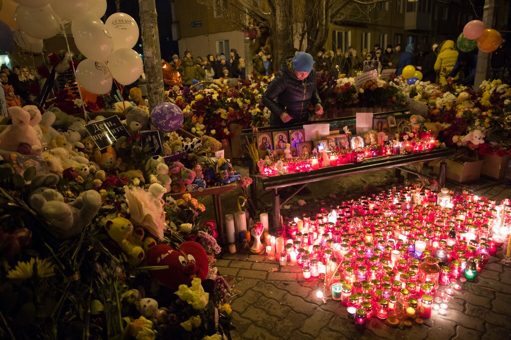 A woman lights candles by a floral tribute for the victims of Sunday's fire in a multi-story shopping center in the Siberian city of Kemerovo, about 3,000 kilometers (1,900 miles) east of Moscow, Russia, Monday, March 26, 2018. Russian officials say that fire escapes were blocked and a PA system was turned off during a fire at a shopping mall in a Siberian city that killed over 60 people. Witnesses reported no alarms and no staff to help them leave the Winter Cherry mall in Kemerovo. (AP Photo/Sergei Gavrilenko)