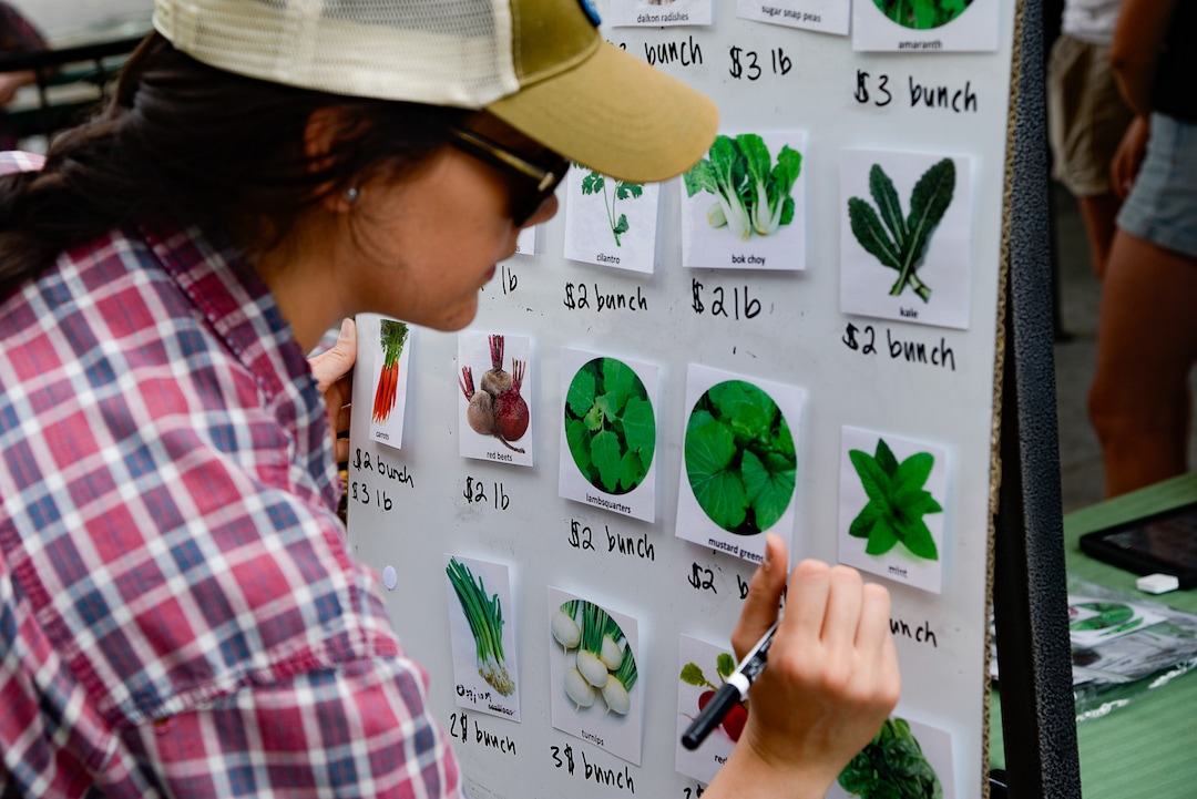 (Francisco Kjolseth  |  The Salt Lake Tribune)   Mariah Leick updates the board with the daily price for vegetables for the Sunnyvale Farmers Market at 4013 S. 700 West, which draws a weekly refugee clientele on Saturday, July 13, 2019, selling food grown exclusively by refugees living in Utah.