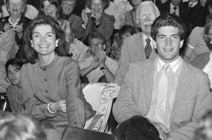 FILE - In this June 6, 1983 file photo, Jacqueline Kennedy Onassis, left, and her son John F. Kennedy Jr., wait to hear a speech by Sen. Edward Kennedy at Brown University in Providence, R.I. Brown University said Friday, Oct. 13, 2017, the college application of John F. Kennedy Jr. that is now up for auction was stolen, and it wants the documents back. The website MomentsInTime.com put an $85,000 price tag on a collection of documents, including Kennedy's application and letters from his mother discussing his time at Brown. (AP Photo/Peter Southwick, File)