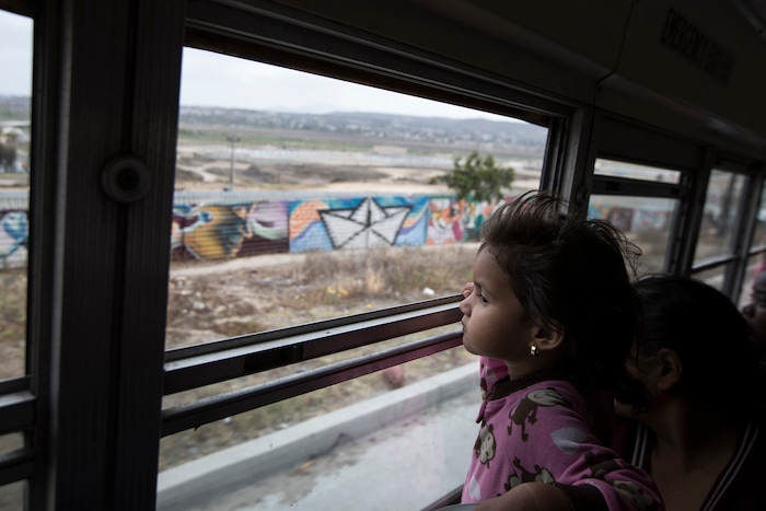 A Central American child who is traveling with a caravan of migrants, peers at the border wall from a bus carrying the group to a gathering of migrants living on both sides of the border, in Tijuana, Mexico, Sunday, April 29, 2018. U.S. immigration lawyers are telling Central Americans in a caravan of asylum-seekers that traveled through Mexico to the border with San Diego that they face possible separation from their children and detention for many months. They say they want to prepare them for the worst possible outcome. (AP Photo/Hans-Maximo Musielik)