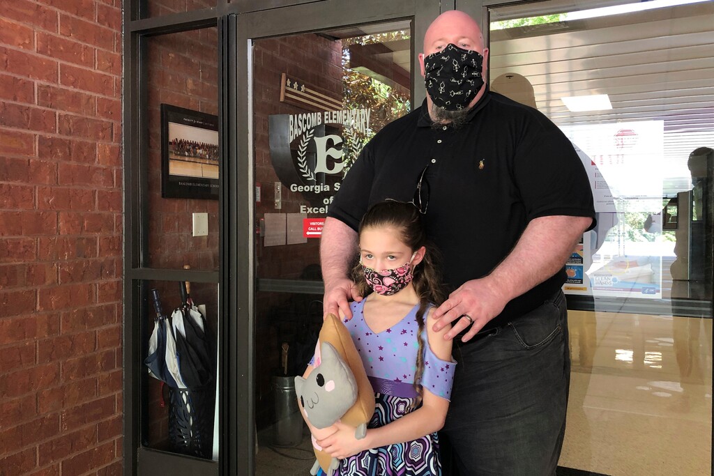 (Jeff Amy | The Associated Press) John Barrett and his daughter Autumn pose for photos outside Bascomb Elementary School in Woodstock, Ga., Thursday, July 23, 2020. Barrett says he will educate his daughter virtually and keep her out of in-person classes in Cherokee County schools, even though he's worried she will fall behind on her special education plans, because of concerns about COVID-19's spread. Cherokee County, near Atlanta, is one of many districts nationwide that gave parents a choice between in-person and all-online classes this fall.