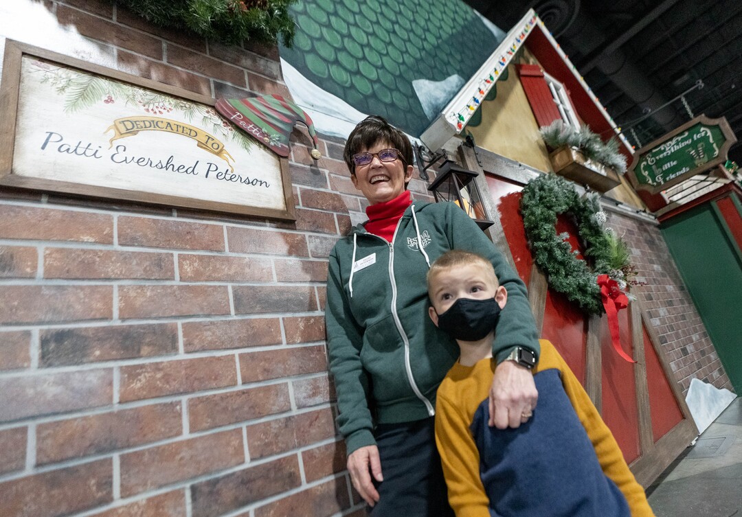 (Francisco Kjolseth | The Salt Lake Tribune) Patti Peterson is joined by her grandson Blake Petty, 5, outside the elf emporium storefront, built by her family, donated in her honor to the Festival of Trees, which is virtual again this year at the Mountain America Expo Center in Sandy on Tuesday, Nov. 30, 2021. Peterson who has terminal cancer wanted to have an influence on the festival for years to come.