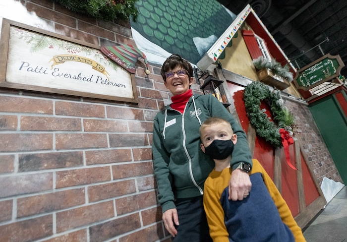 (Francisco Kjolseth | The Salt Lake Tribune) Patti Peterson is joined by her grandson Blake Petty, 5, outside the elf emporium storefront, built by her family, donated in her honor to the Festival of Trees, which is virtual again this year at the Mountain America Expo Center in Sandy on Tuesday, Nov. 30, 2021. Peterson who has terminal cancer wanted to have an influence on the festival for years to come.