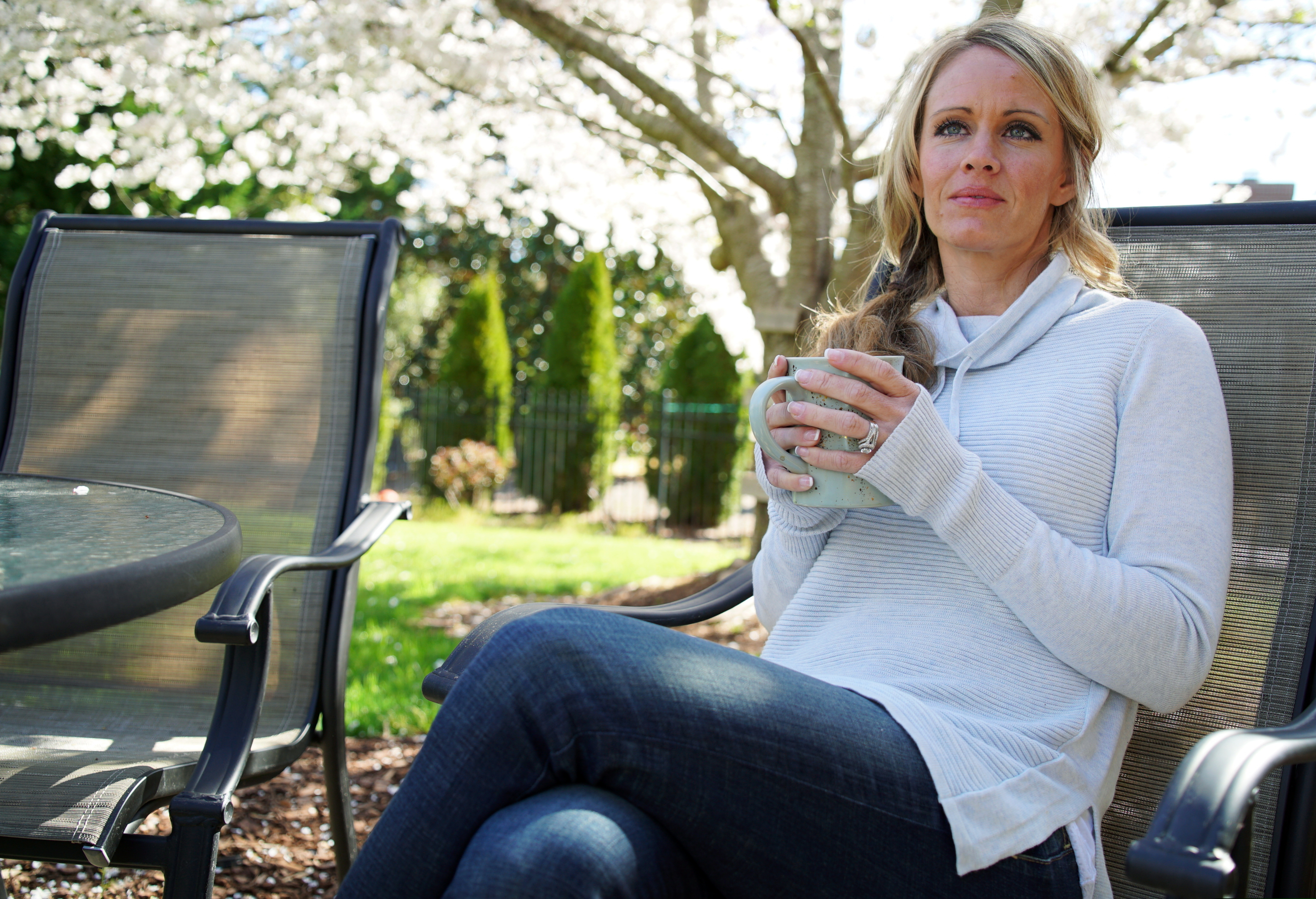 In this Wednesday, March 27, 2019, photo, Kacey Ruegsegger Johnson enjoys a coffee in a light spring breeze in the back yard of her home in Cary, N.C. For the last 20 years since she was injured in the Columbine High School attack, she has lived with post-traumatic stress disorder, along with physical pain.  Now a mother of four, she has worked hard not to pass that fear on to her children. (AP Photo/Allen G. Breed)