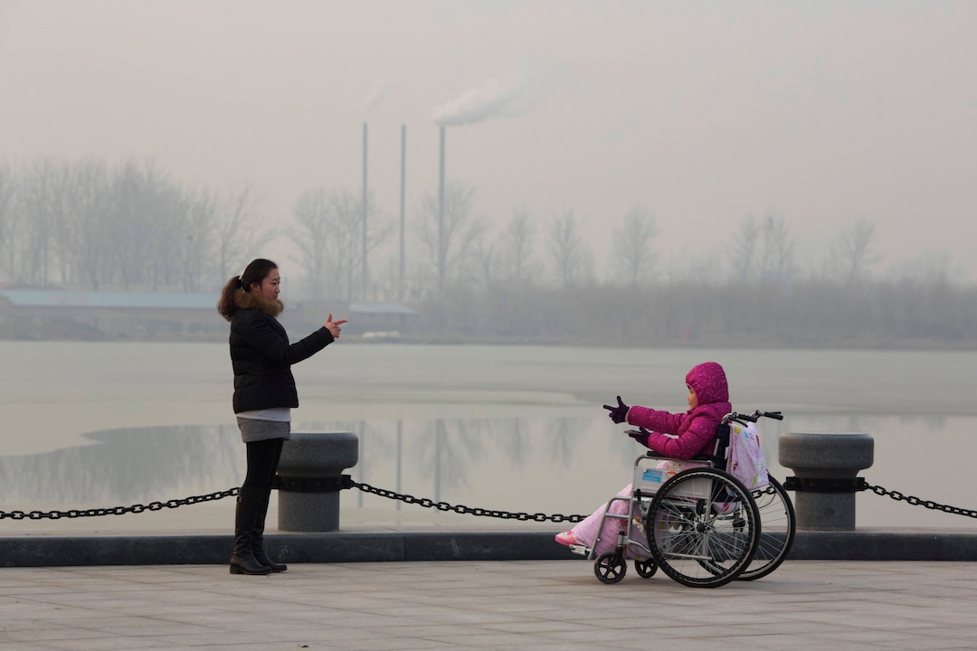 FILE - In this Dec. 12, 2015, file photo, visitors to a park gestures at each other near chimneys spewing smoke in Beijing. Environmental pollution - from filthy air to contaminated water - is killing more people every year than all war and violence in the world. One out of every six premature deaths in the world in 2015 - about 9 million - could be attributed to disease from toxic exposure, according to a major study released Thursday, Oct. 19, 2017 in The Lancet medical journal. (AP Photo/Ng Han Guan, File)