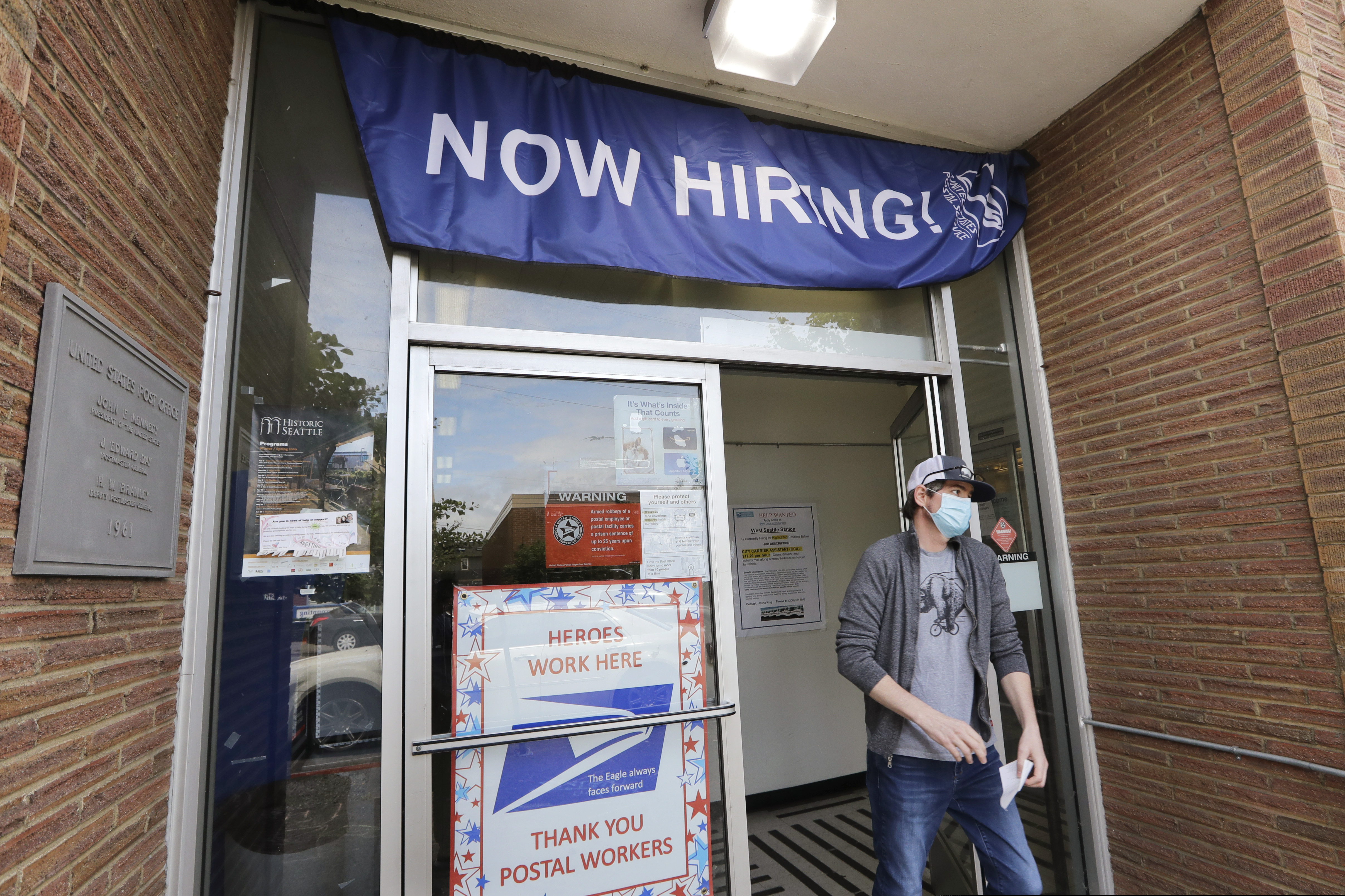 (Elaine Thompson | AP) In this photo taken Thursday, June 4, 2020, a customer walks out of a U.S. Post Office branch and under a banner advertising a job opening, in Seattle.