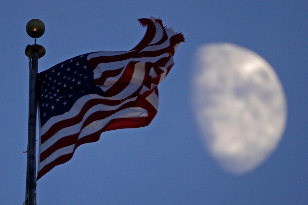 (Charlie Riedel | AP file photo) A flag flies in the wind above City Hall as the waxing gibbous moon passes behind clouds overhead in Kansas City, Mo., on June 29, 2020.