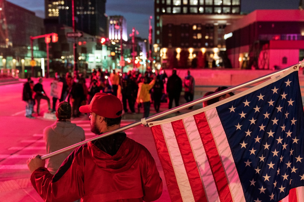 (David Goldman | The Associated Press) A Trump supporter demonstrating against the election results holds an American flag as counter protestors stand across the street outside the central counting board at the tcf Center in Detroit, Thursday, Nov. 5, 2020.