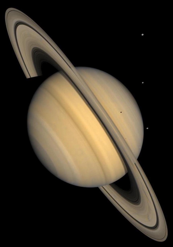 (Credit: Courtesy of NASA/Jet Propulsion Laboratory) This approximate natural-color image shows Saturn, its rings, and four of its icy satellites. Three satellites (Tethys, Dione, and Rhea) are visible against the darkness of space, and another smaller satellite (Mimas) is visible against Saturn's cloud tops very near the left horizon and just below the rings. This image was synthesized from images taken in Voyager's blue and violet filters and was processed to recreate an approximately natural color and contrast.