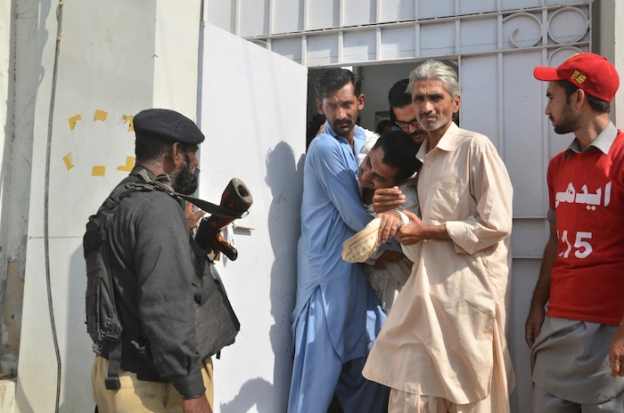 People comfort a relative of a police officer killed during a shootout at the Chinese Consulate in Karachi, Pakistan, Friday, Nov. 23, 2018. Armed separatists stormed the Chinese Consulate in Pakistan's southern port city of Karachi on Friday, triggering an intense hour-long shootout during which two police officers and all three assailants were killed, Pakistani officials said. (AP Photo/Shakil Adil)