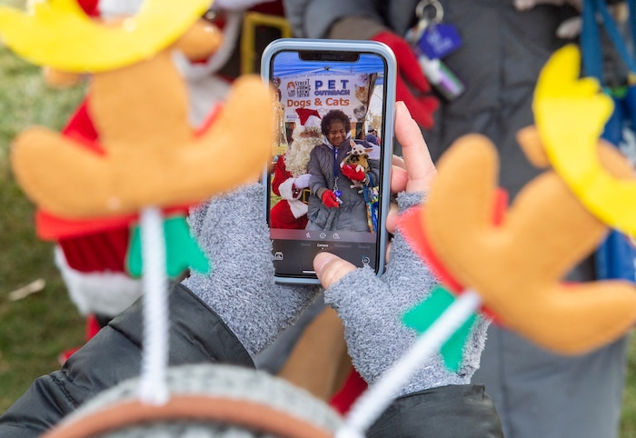 (Rick Egan  |  The Salt Lake Tribune)    Volunteer, Jenny Espindola takes photos of Laura Sykes with her dog Snowflake, at the Street Dawg Crew Christmas outreach at Liberty Park Sunday.  The Street Dawg Crew supports the homeless and their pets every Sunday at Pioneer Park.  For today's Christmas Outreach, the Street Dawg Crew passed out food and gift bags for humans and animals, and also offered a photo opportunity with Santa. Sunday, Dec. 22, 2019.